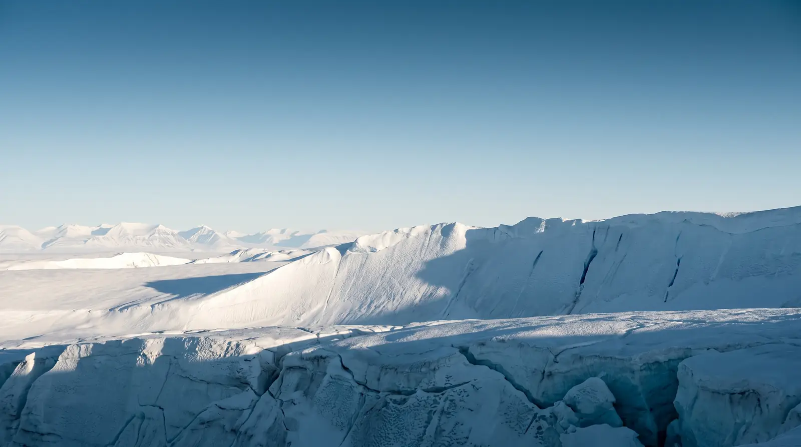 Arktisk isbre med sprekker og fjelltopper i bakgrunnen.